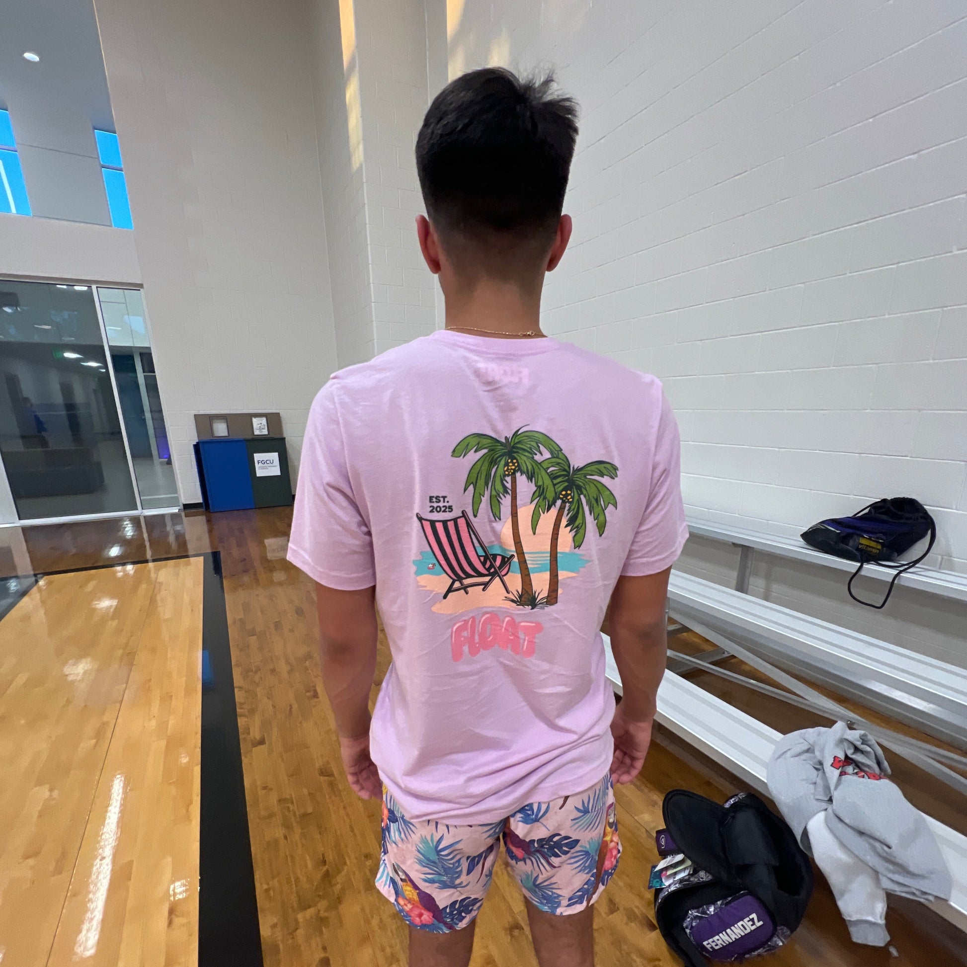 Person wearing a pink t-shirt with palm tree design and colorful shorts in a room.
