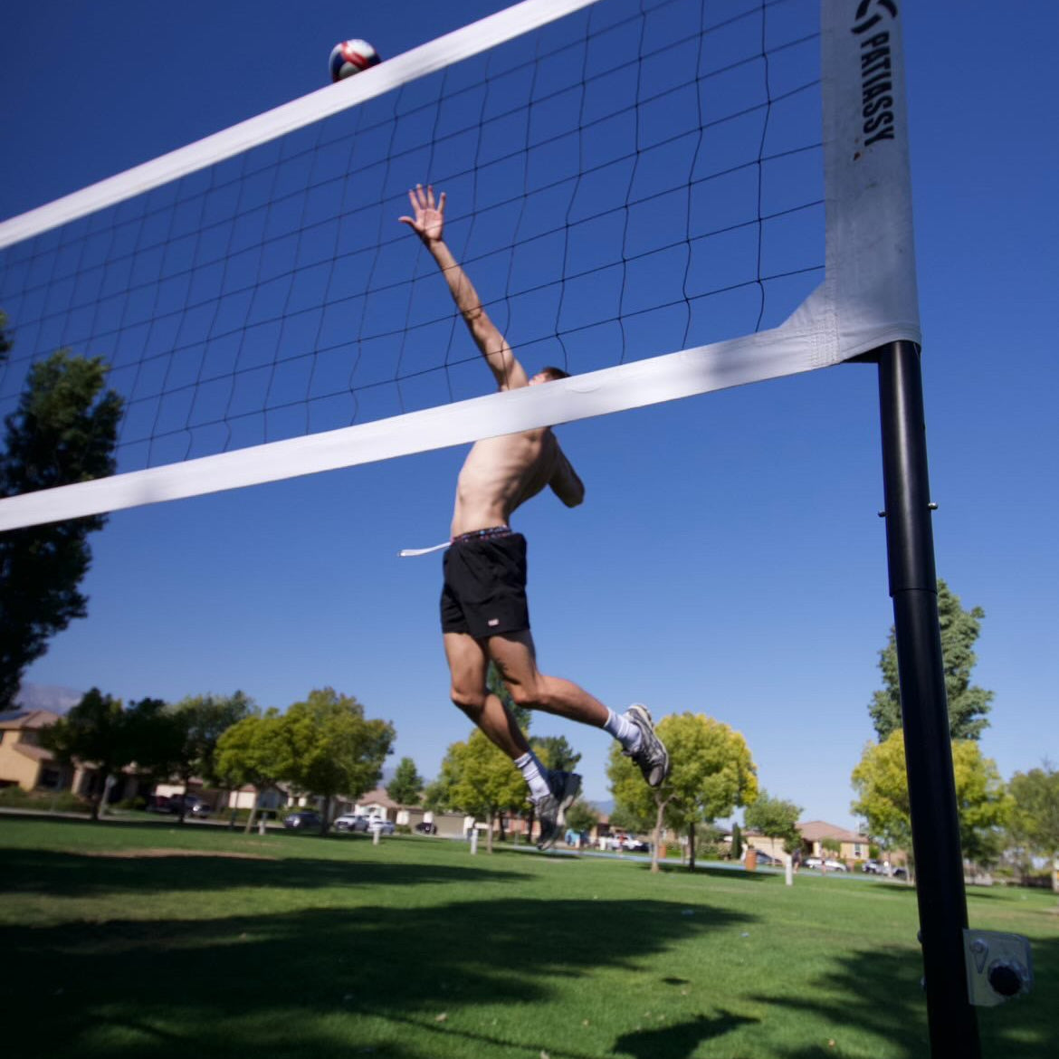 Man playing volleyball jumping over a net on a sunny day
