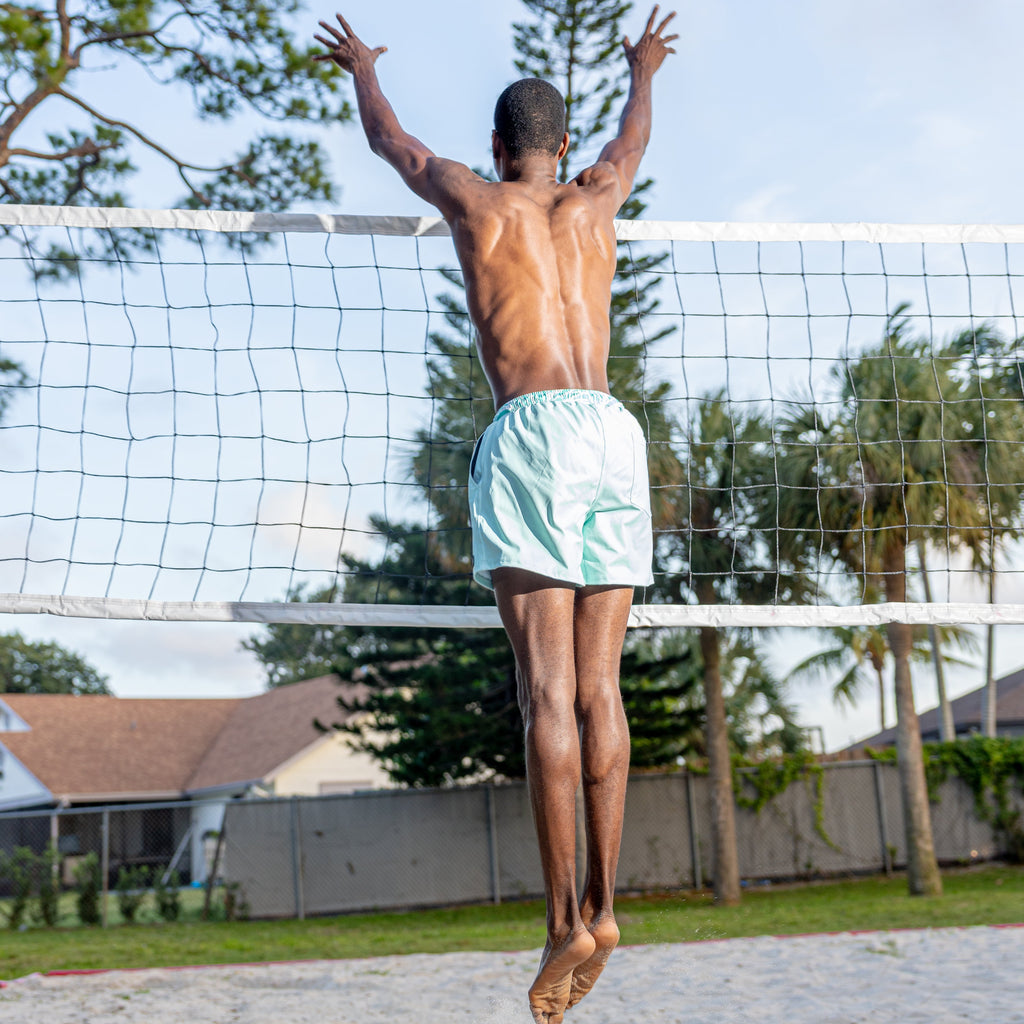 Man jumping over a volleyball net with trees and houses in the background