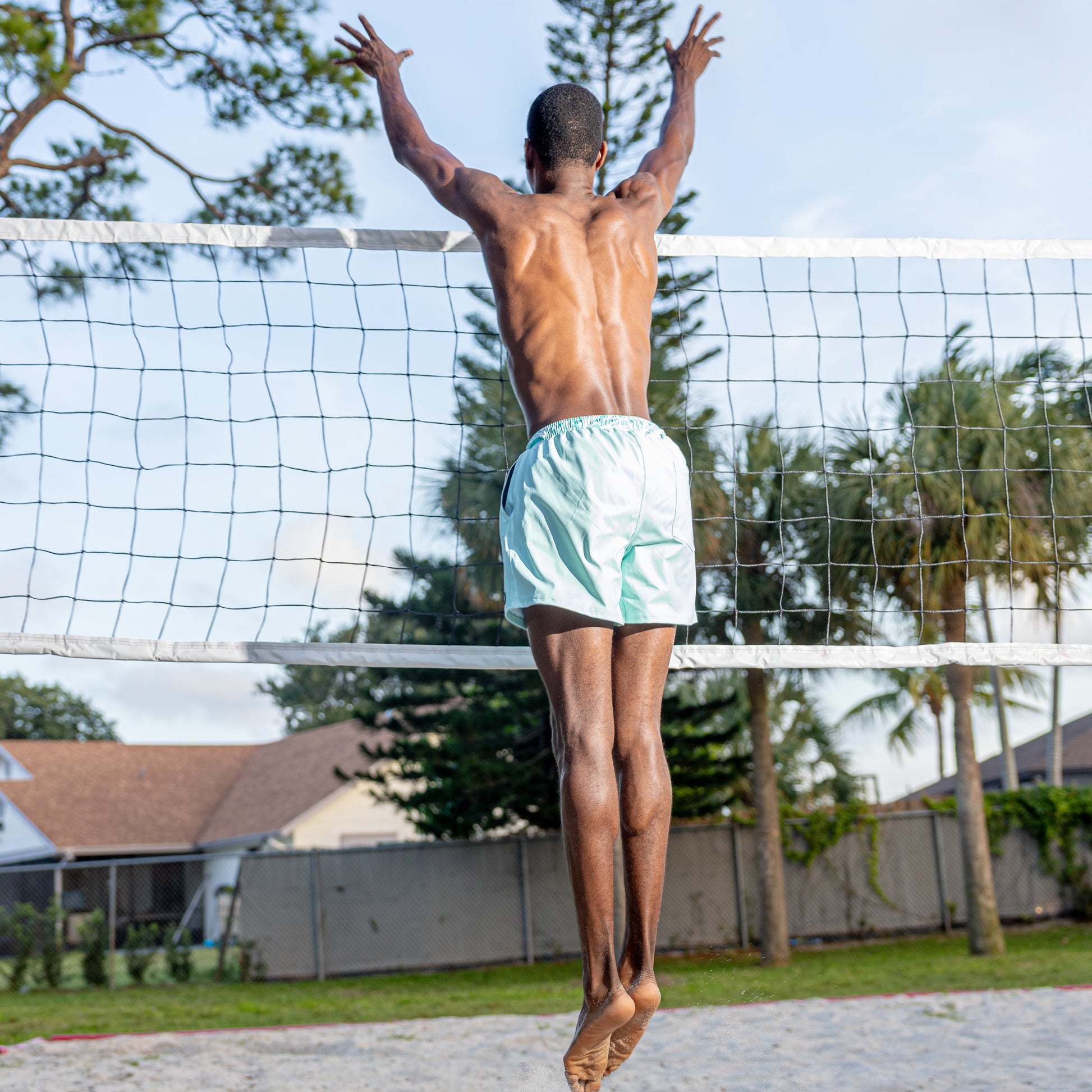 Man jumping over a volleyball net with trees and houses in the background