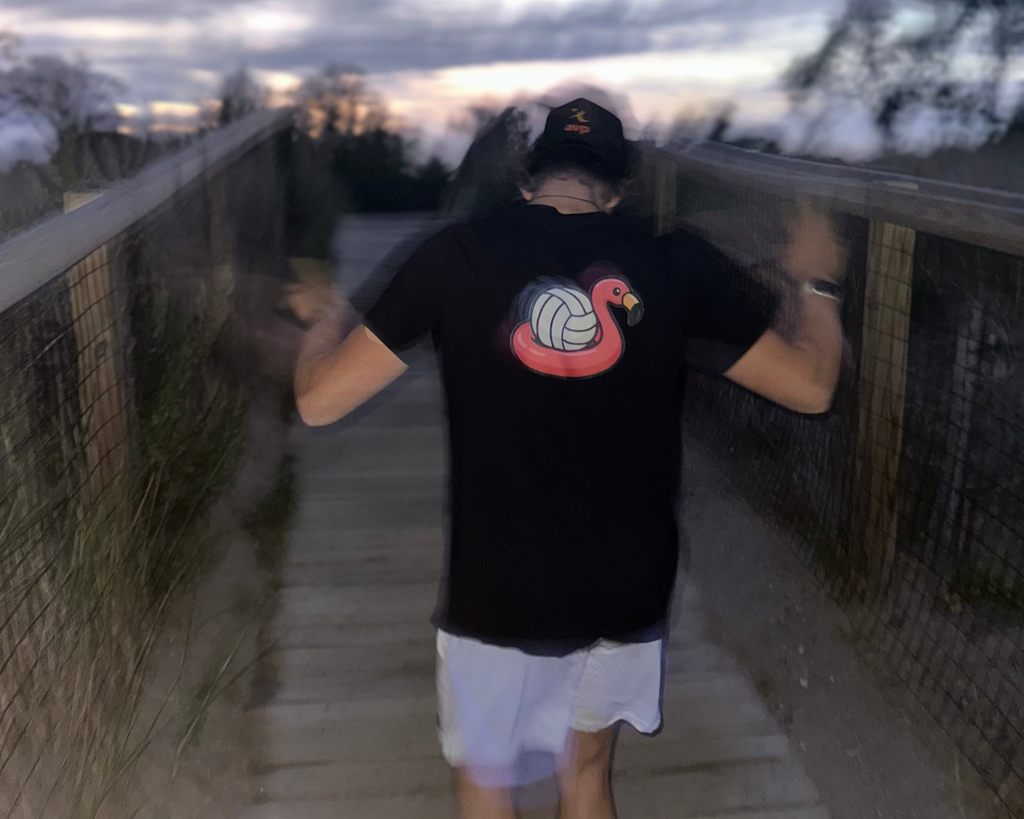 Person wearing a black t-shirt with a colorful design on a wooden walkway at dusk.