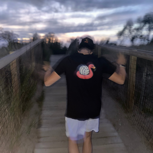 Person wearing a black t-shirt with a colorful design on a wooden walkway at dusk.