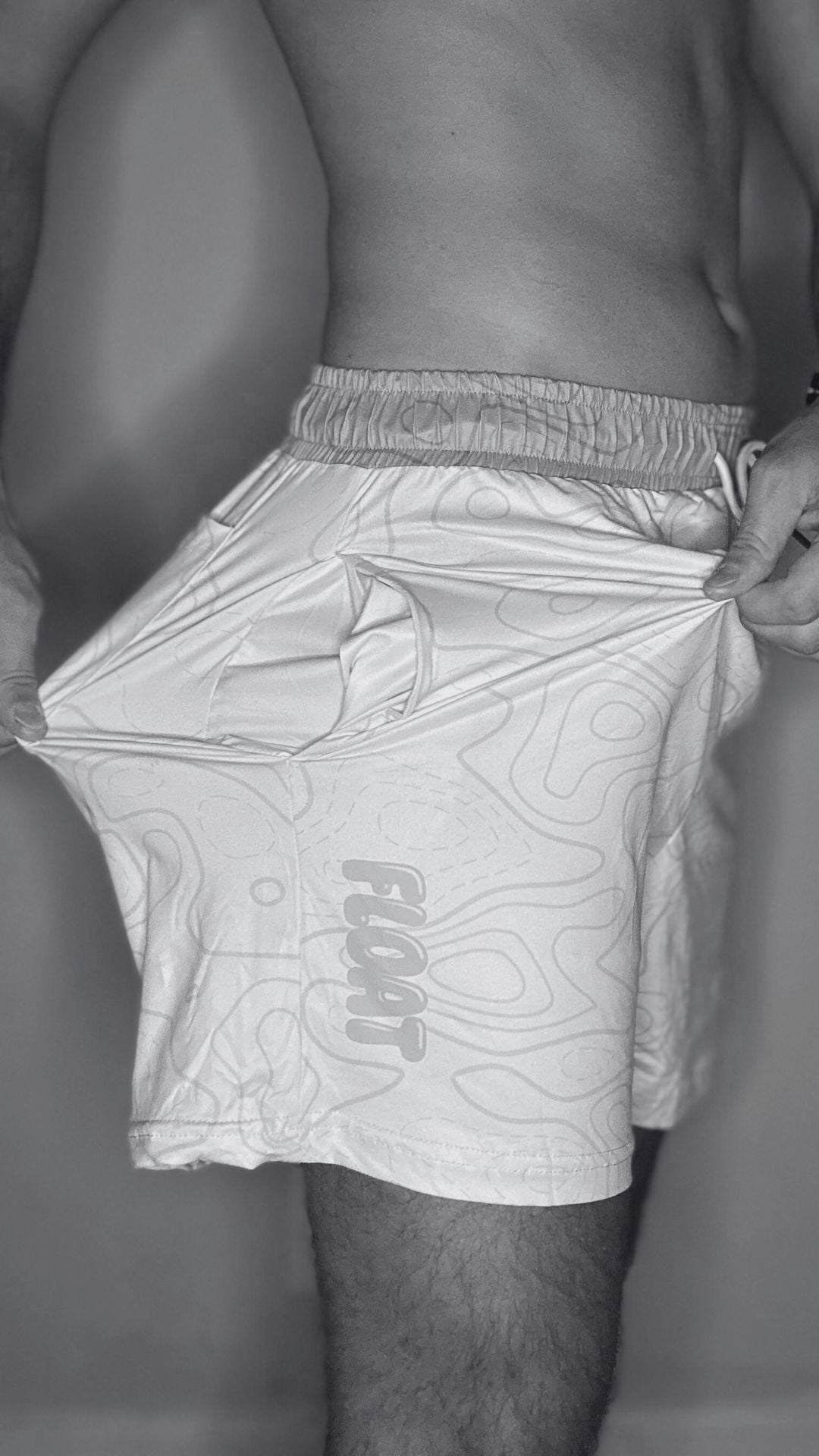 Person wearing light gray swim shorts with a brand logo on a neutral background