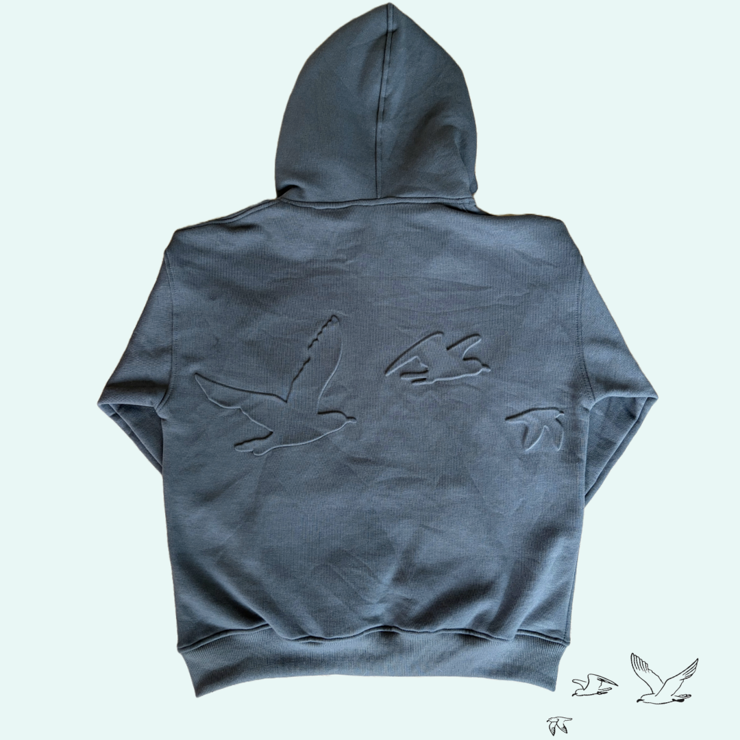 A dark charcoal gray hoodie shown from the back, featuring a large tonal embossed bird design across the upper back. The hoodie is displayed flat against a very pale mint green background.