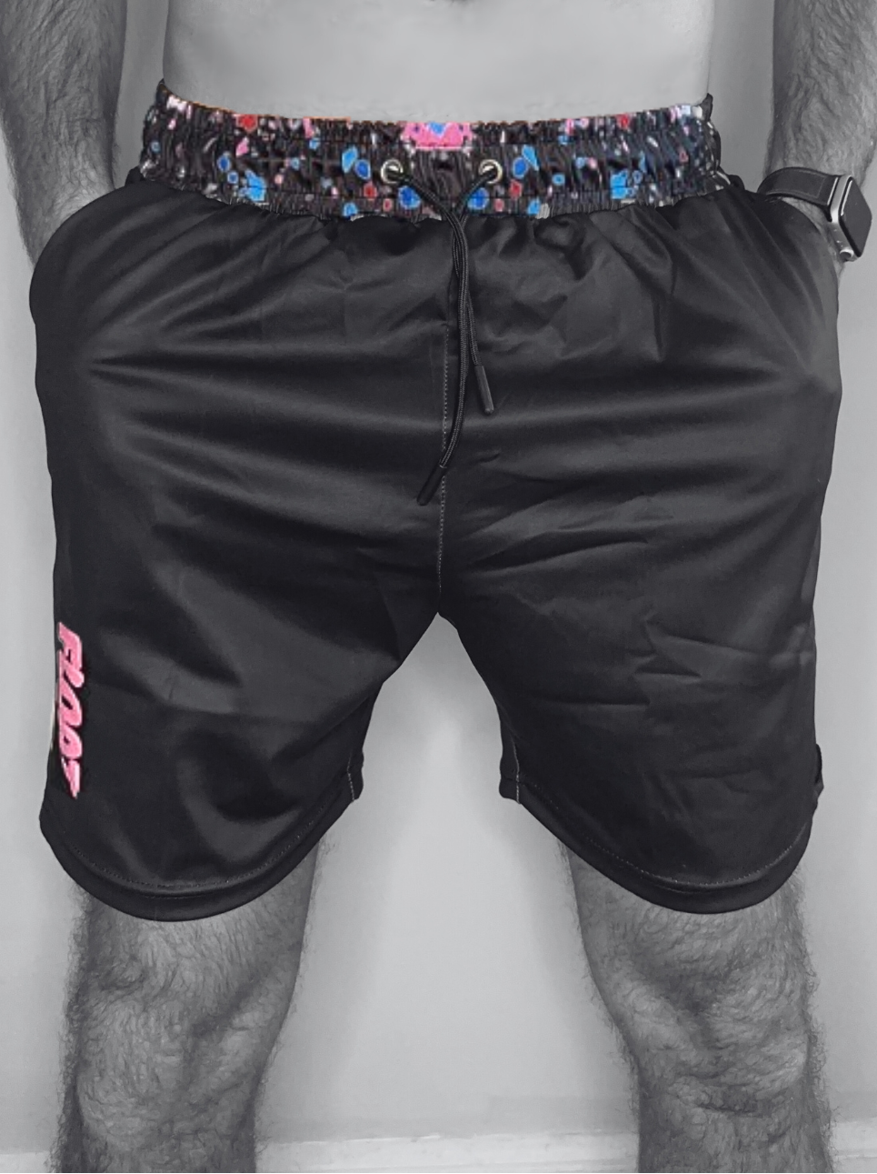 Black shorts with colorful waistband and pink logo on a plain background