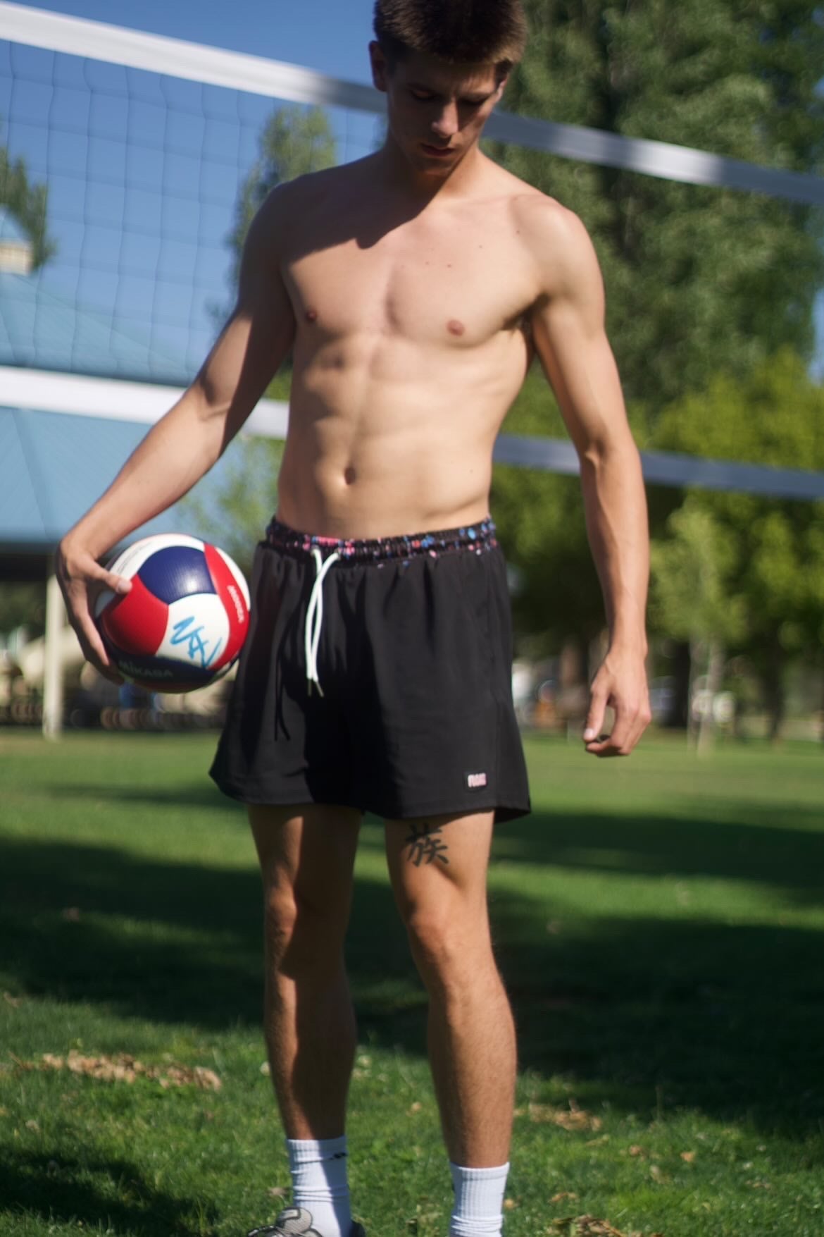 Man holding a volleyball on a grassy field with a net in the background