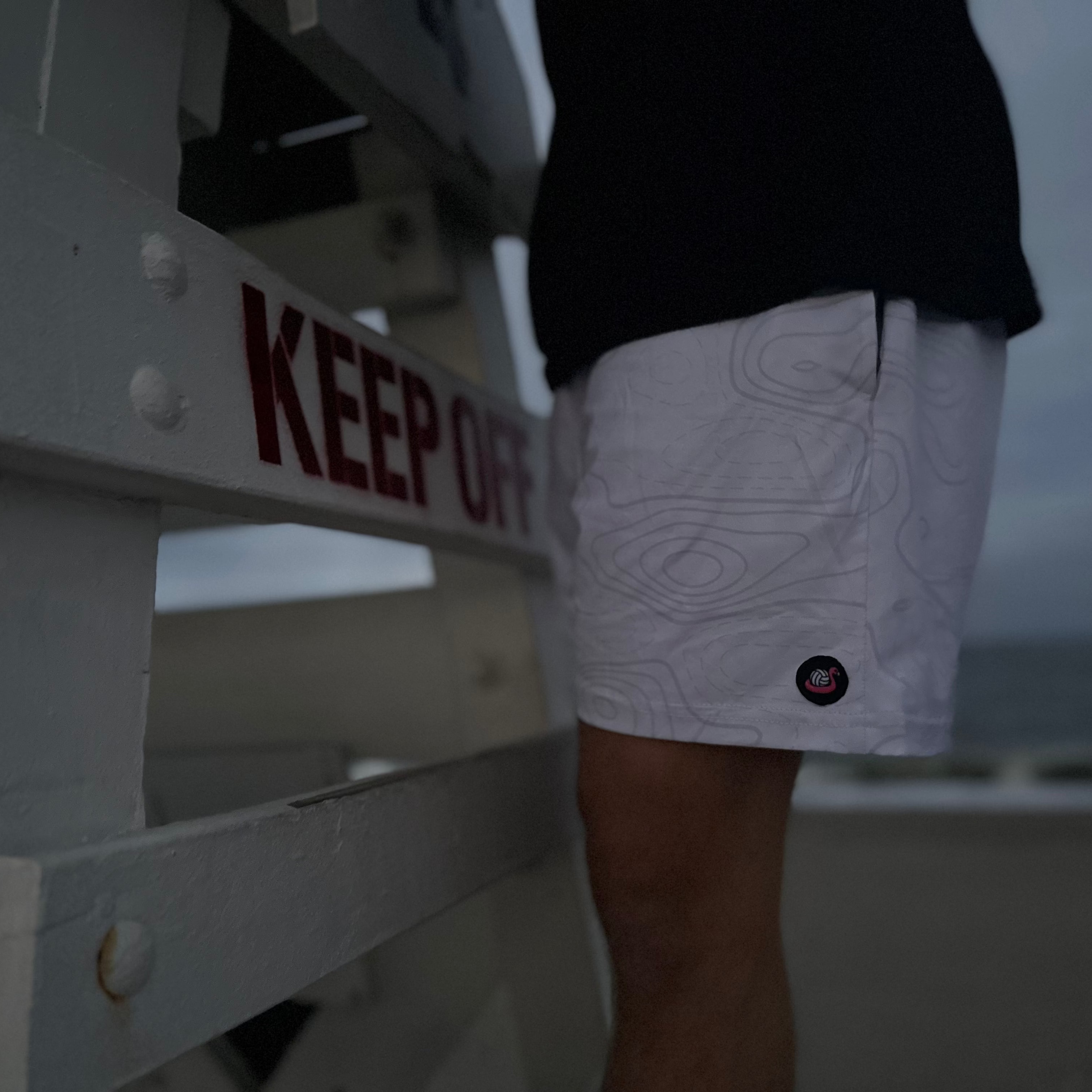 Person wearing white shorts with a pattern, standing next to a 'KEEP OFF' sign on a beach.