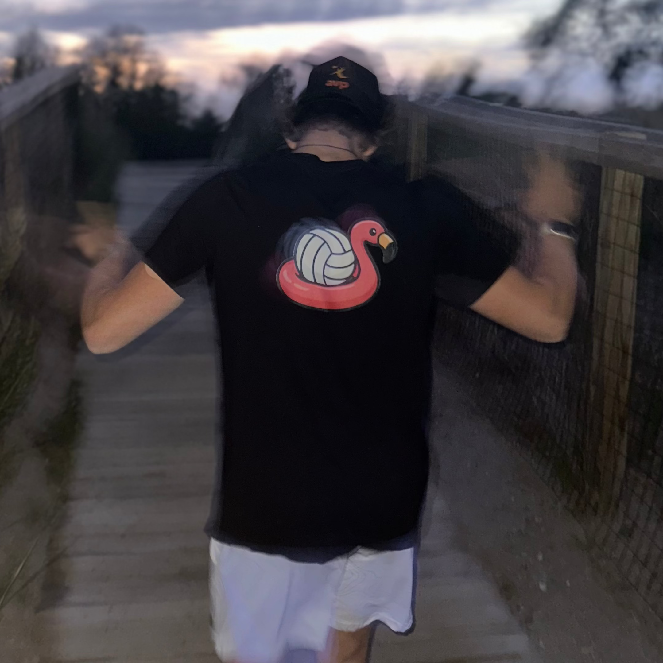 Person wearing a black t-shirt with a colorful design on a wooden walkway at dusk.